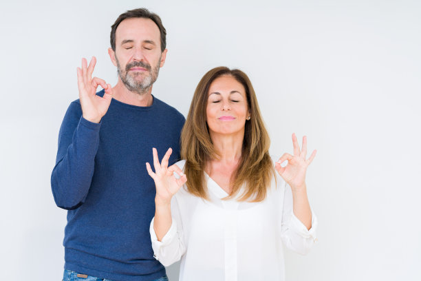 美丽的中年夫妇在孤独的背景下放松，微笑着闭上眼睛，用手指做冥想手势。瑜伽的概念。图片下载