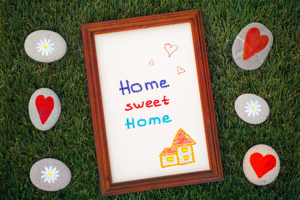 家温馨的家画在木框架上的绿草背景与一些鹅卵石与雏菊和心。图片下载