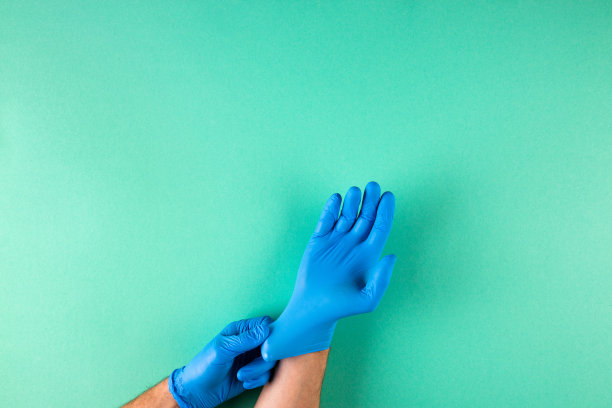 男性双手戴着蓝色乳胶手套，青绿色背景图片下载