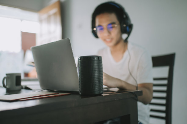 一名亚裔中国少年在厨房餐桌上与他的虚拟助手智能音箱一边做作业，一边通过网络软件与所有同学在线聊天图片下载