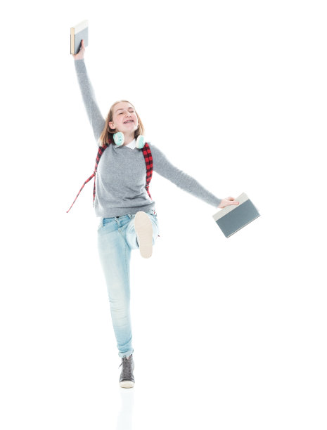 z一代年轻女大学生穿着暖和的衣服，拿着书，戴着耳机走在白色背景前图片下载