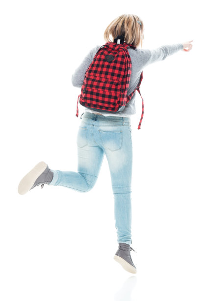 z一代女高中生背着背包，拿着课本，戴着耳机，在白色背景前跳跃图片下载