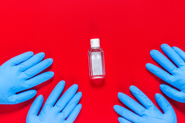 红色背景上的蓝色医用手套和消毒剂瓶。防范危险病毒。病毒感染的季节。图片下载