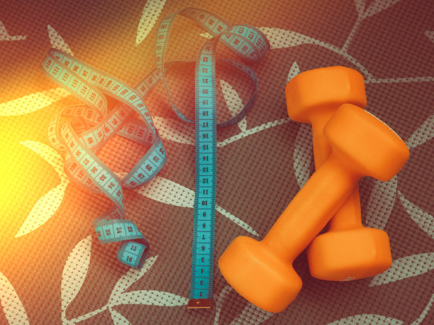 艺术照片与测量卷尺控制身体体积和橙色哑铃健身背景的阳光眩光图片下载