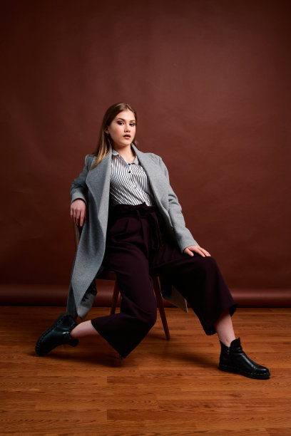 独立的年轻女子在照相馆摆姿势。穿着经典套装和灰色外套的漂亮年轻女性。图片下载