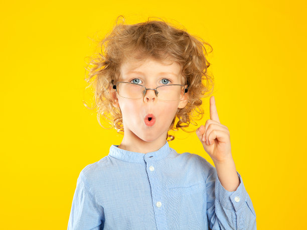 一个漂亮的卷发、戴着金色眼镜的男孩惊讶地抬起一根手指，把嘴唇像管子一样地拉了出来。图片下载