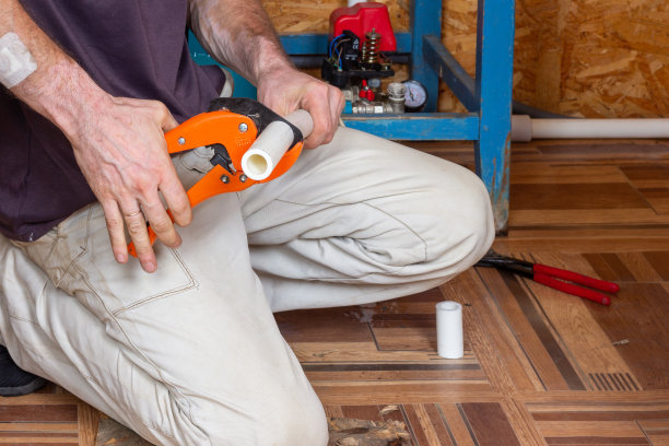 安装暖气或供水系统。一名男水管工用剪刀切割聚丙烯塑料管来焊接水管图片下载