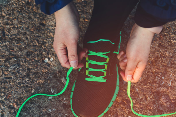 女人们双手系上运动鞋的鞋带，在阳光下在柏油路上积极慢跑或散步，俯视图。慢跑，跑步，健身，健身房的概念图片下载