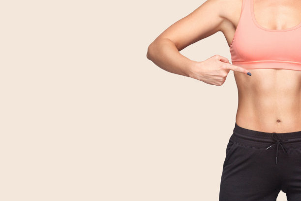 特写的健康的女人穿着运动紧身上衣和裤子指向自己，显示苗条的运动员的身体与训练有素的肌肉图片下载