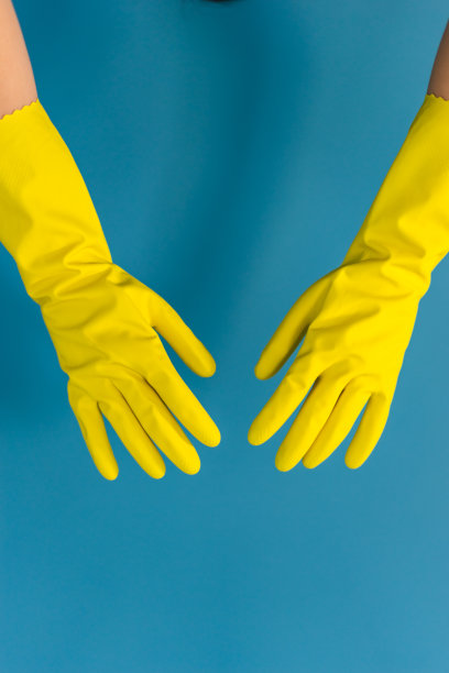 近手的未知白人妇女女女孩举起的手与保护性的黄色橡胶手套用于清洁或消毒对蓝色的墙壁背景在天图片下载