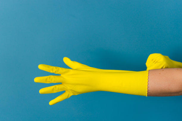 近距离观察不知名白人妇女女女孩的手，戴着调整，手持保护性黄色橡胶手套，以清洁或消毒对蓝色的墙壁背景在天图片下载