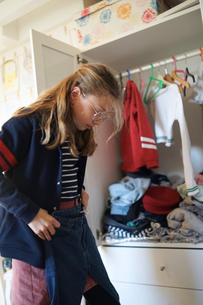 小女孩在壁橱里挑选自己的衣服。衣架和抽屉上有很多衣服可供选择，孩子在衣柜前想着要穿什么。图片下载