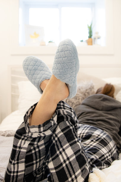 女人懒洋洋地躺在床上，穿着睡衣和舒适的蓝色拖鞋。图片下载
