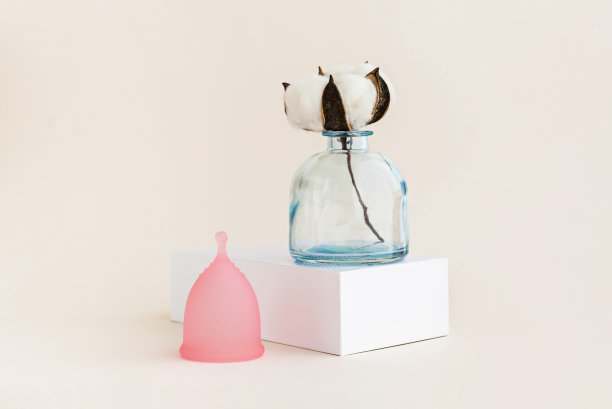 月经杯与白色棉花花在柔和的背景。最小的单色创意图片。图片下载