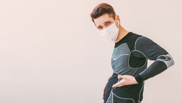 困惑的运动员在医疗面罩抱着他的大胖肚子图片下载