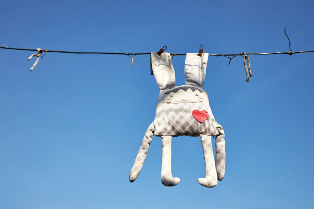 遗忘的旧褪色的玩具兔子挂在晾衣绳上的背景蓝色的天空图片下载