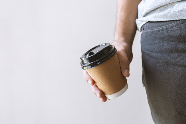 特写男性的手拿着一个热咖啡杯与软焦点和在背景过光图片下载