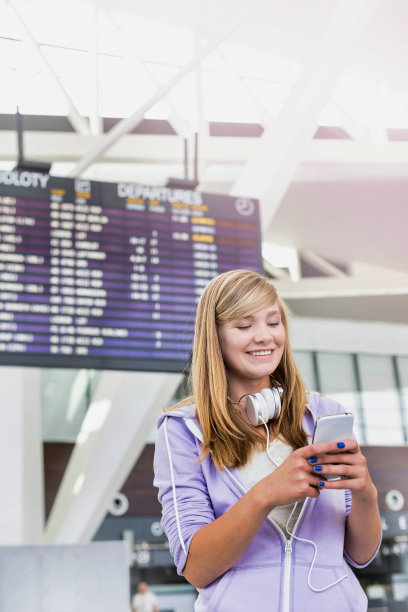 年轻美丽的少女在机场使用带镜头光晕的智能手机的肖像图片下载