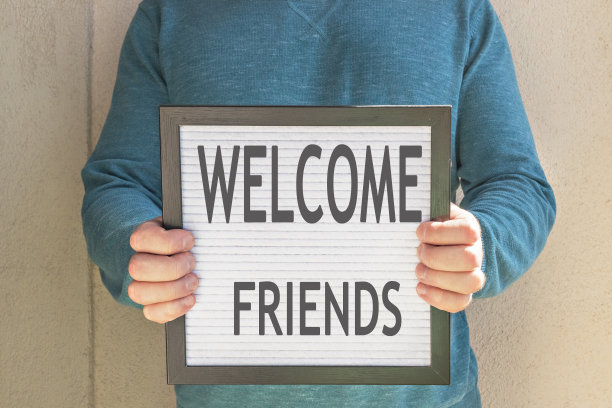 一名男子举着一张写着“欢迎朋友们”的标语。隔离的终结。酒店、咖啡馆、当地商店、服务业主在冠状病毒大流行和隔离后接待客人。图片下载