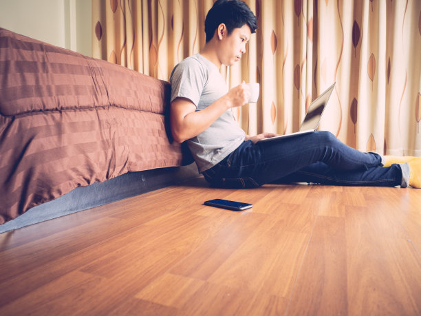 在家工作(WFH)概念。一名男子坐在卧室地板上用笔记本电脑工作。图片下载