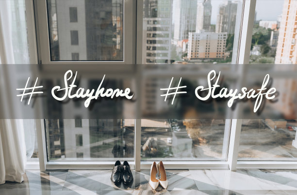 两双鞋，男一双黑，女一双粉，放在大窗户旁边，背景是摩天大楼。题词:#呆在家里，呆在安全的地方。隔离、冠状病毒、COVID-19的概念。标签图片下载