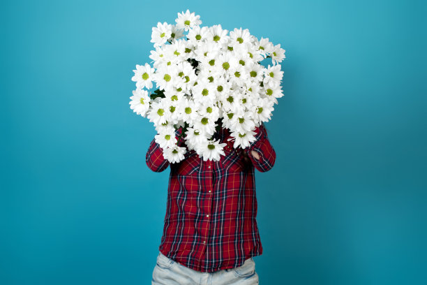 一个穿着红衬衫的女孩在他面前举着一束白色的菊花图片下载