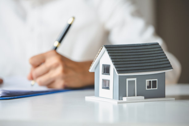 商人和客户正在签署购房协议。手握笔签购合同。灰色屋顶的房子和钥匙彼此靠近。房产抵押购房。图片下载