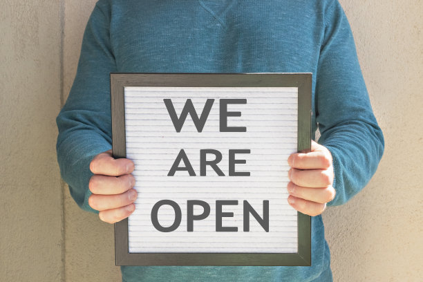 一名男子举着一个牌子，上面写着欢迎短信“我们开门了”。隔离的终结。酒店、咖啡馆、当地商店、服务业主在冠状病毒大流行和隔离后接待客人。图片下载
