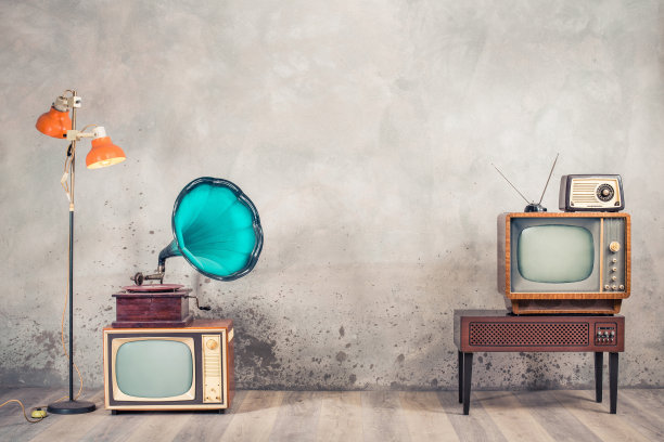 复古的模拟阴极射线管电视机，带有过时放大器的木制电视架，60年代的老式收音机，经典的留声机，落地灯前面是老化的混凝土墙背景。复古风格滤镜照片图片下载
