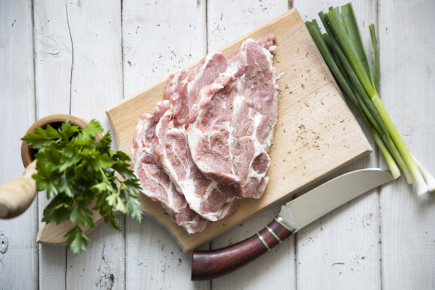 生肉和晚餐的配料。猪里脊肉，里脊肉，放在砧板上，加盐，胡椒粉，欧芹，大蒜。木制白色桌子，拷贝空间顶部视图图片下载