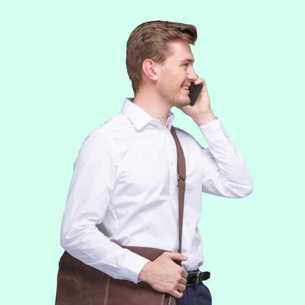 白人年轻男性商务人士站在那里，背着肩包，拿着包，使用手机图片下载