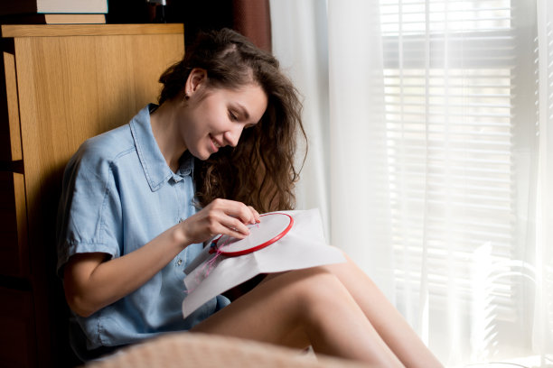 微笑的女孩坐在窗边绣十字。爱好图片下载