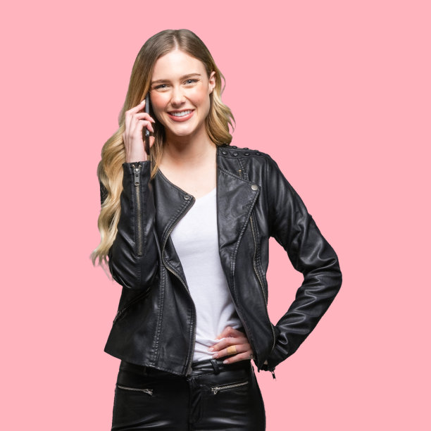 白人女性穿着皮夹克，在有色背景前使用智能手机图片下载