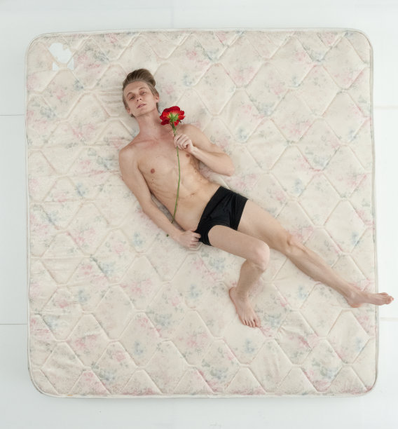 男性穿着内衣，手捧一朵花，在卧室的白色背景前放松图片下载