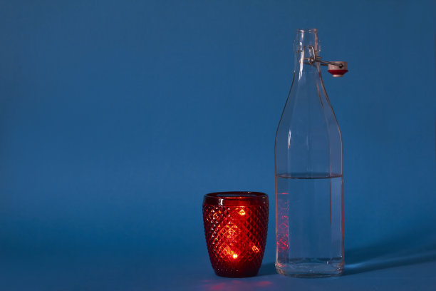 玻璃瓶装清水和红色玻璃在蓝色背景，选择性聚焦图片下载