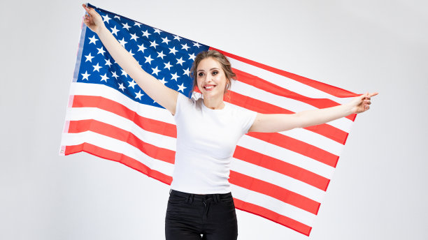 时尚年轻女子的肖像在工作室白色衬衫与灰色孤立的背景。概念与复制空间。她手里拿着一面美国国旗图片下载