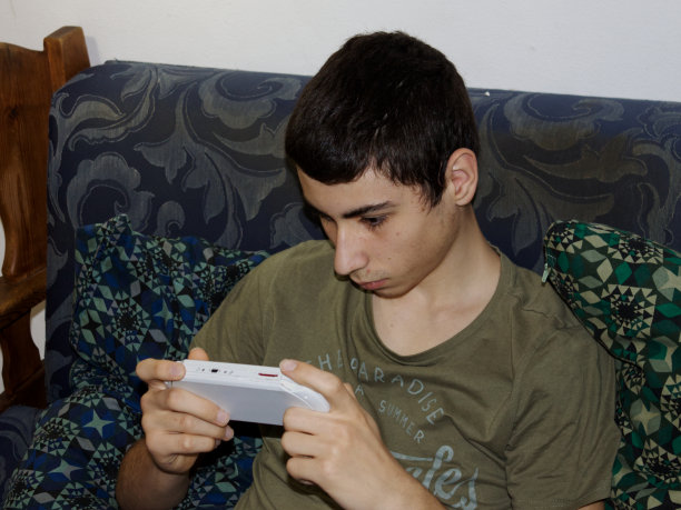 一个白人男孩在沙发上玩便携式游戏机图片下载