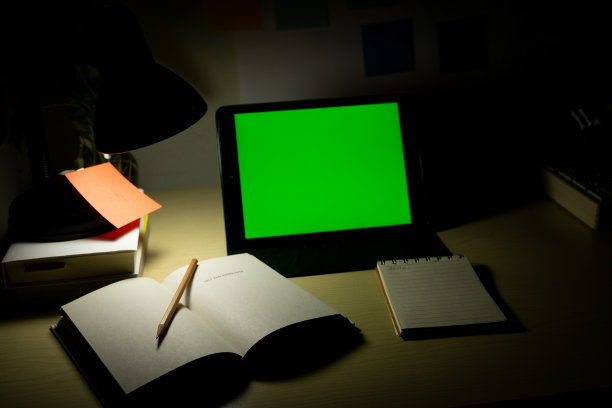 写字台上放着空白屏幕的写字板，旁边放着书本和文具。晚上在家办公。COVID-19大流行期间的在线学习和在家工作概念。图片下载