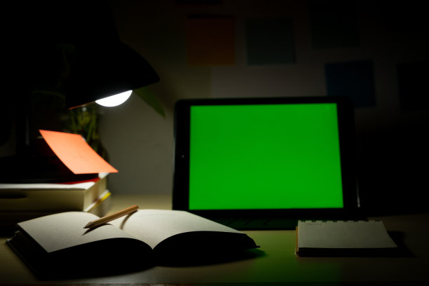 写字台上放着空白屏幕的写字板，旁边放着书本和文具。晚上在家办公。COVID-19大流行期间的在线学习和在家工作概念。图片下载