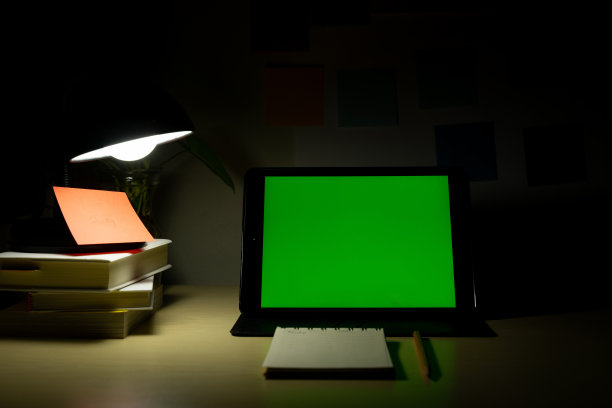 写字台上放着空白屏幕的写字板，旁边放着书本和文具。晚上在家办公。COVID-19大流行期间的在线学习和在家工作概念。图片下载