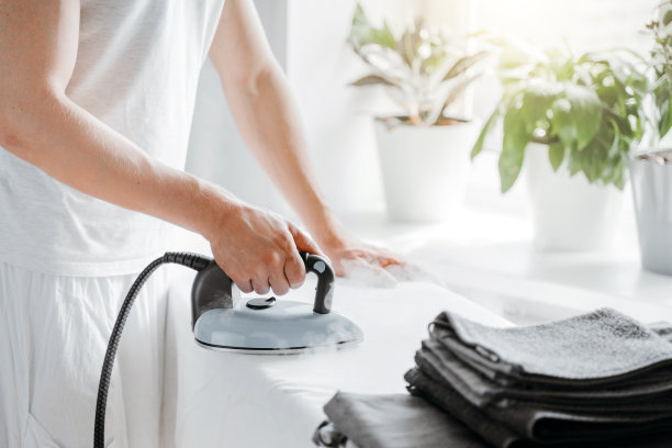 男人在家里的熨衣板上熨烫床单。图片下载