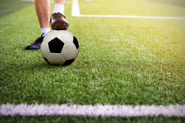 足球鞋和足球在绿色的草地上，足球运动员的脚开始比赛。图片下载