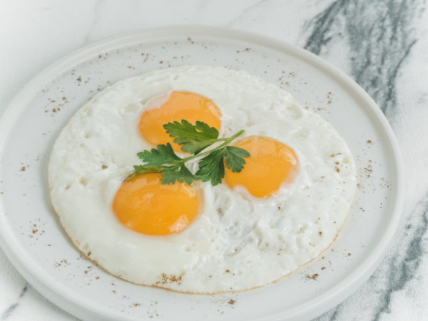 早餐是在白色大理石背景上的白色盘子上煎的三个鸡蛋。装饰着欧芹。芝士炒鸡蛋。菜单的照片。图片下载