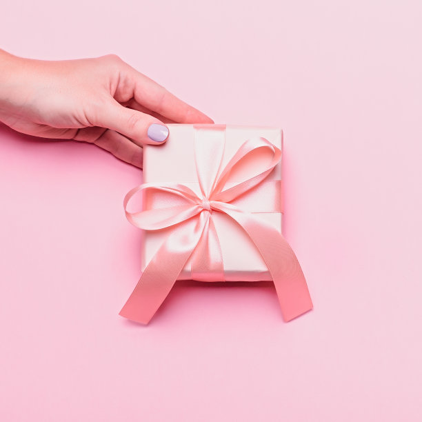 一个拿着粉色礼盒的女人，背景是彩色的。母亲节或妇女节贺卡的时尚颜色，俯视图图片下载