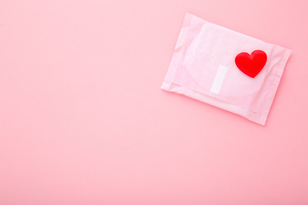 明亮的红色心形卫生巾包装在浅粉红色的桌子背景。柔和的颜色。特写镜头。文本的空位置。自顶向下的观点。图片下载