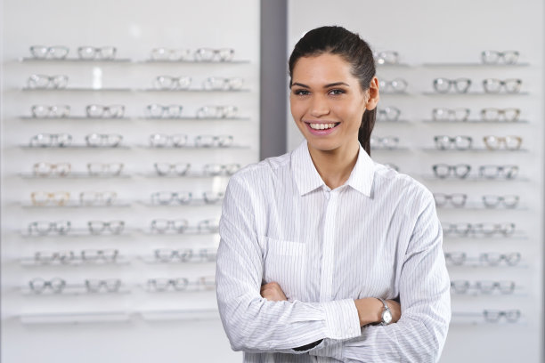 一个美丽的女人的肖像在光学中心微笑着看着相机，高兴的眼科医生的访问和眼镜刚买。图片下载