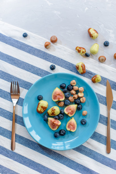 蓝色盘子里装着新鲜成熟的无花果、枣子、蓝莓和生榛子。图片下载
