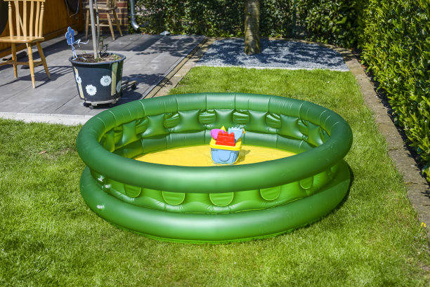 一个为孩子们准备的绿色小家庭游泳池，放在花园的草地上。图片下载