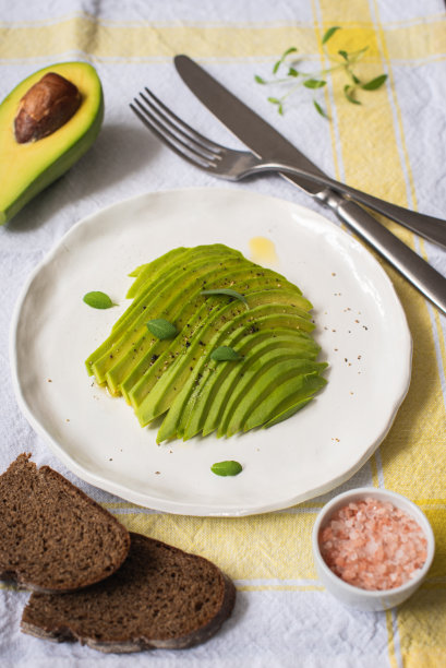 新鲜牛油果切成薄片，放在白盘子里，还有黑麦面包片图片下载