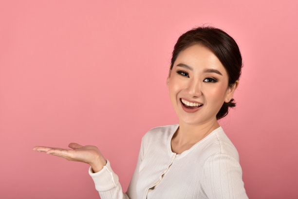 美丽的亚洲女人手打开展示产品的粉红色背景上的广告，快乐的微笑女孩的肖像与复制空间。图片下载